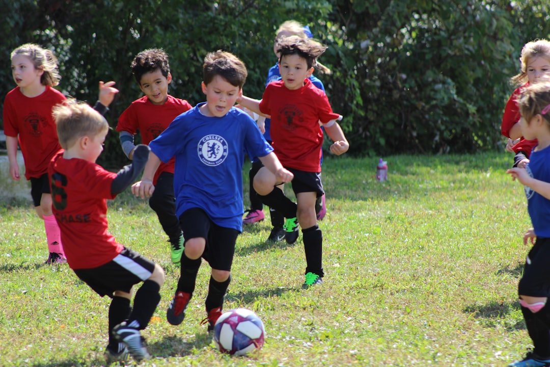 boy-in-red-and-blue-soccer-jersey-kicking-soccer-ball-on-green-grass-field-during-daytime-avgipreokfm