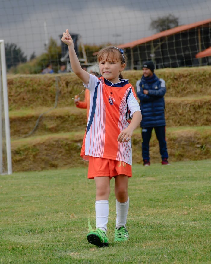 A young girl celebrates during a soccer match on a grassy field. Sport and childhood joy.