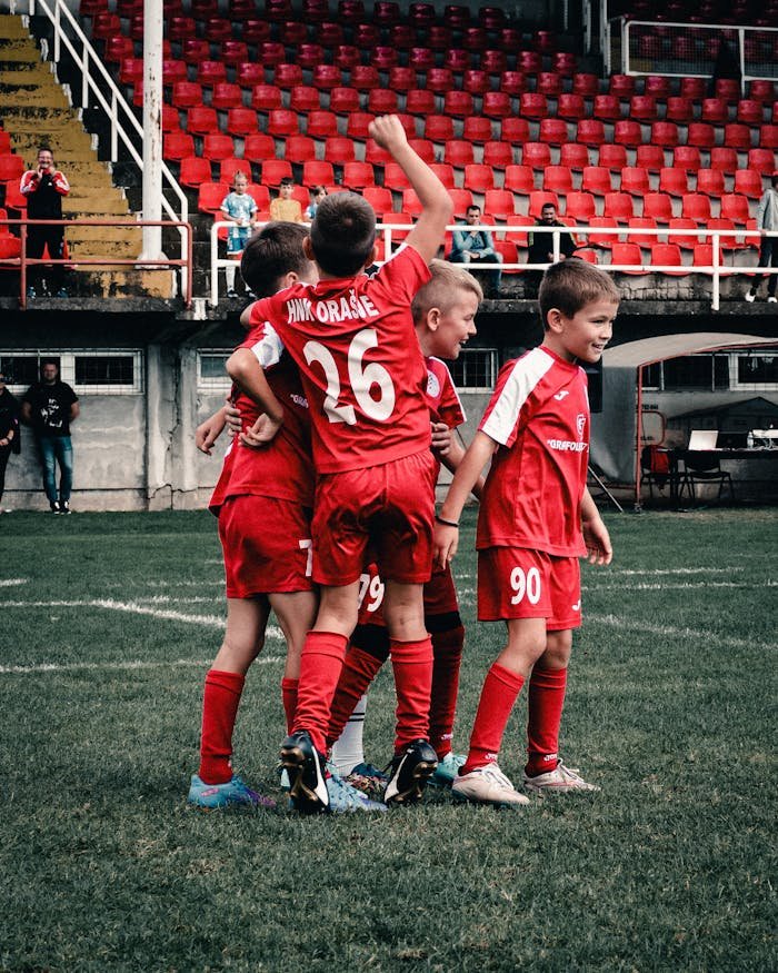 A group of young boys celebrating a success during a football game on a grassy field in Orašje.