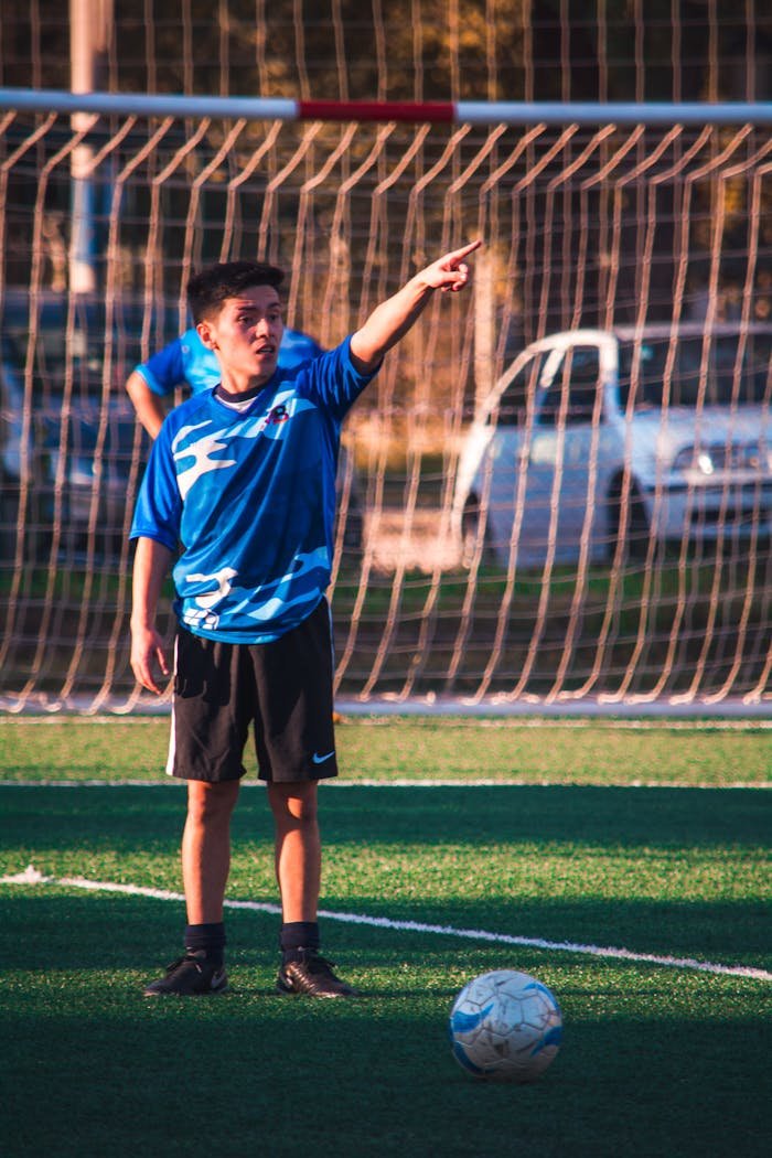 A teenage soccer player in blue jersey directing teammates during a game on a sunny day.
